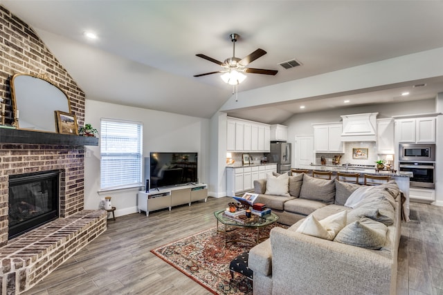 living room featuring lofted ceiling, light hardwood / wood-style flooring, a brick fireplace, and ceiling fan