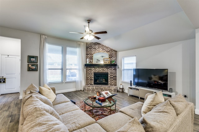 living room with dark wood-type flooring, ceiling fan, vaulted ceiling, and a brick fireplace