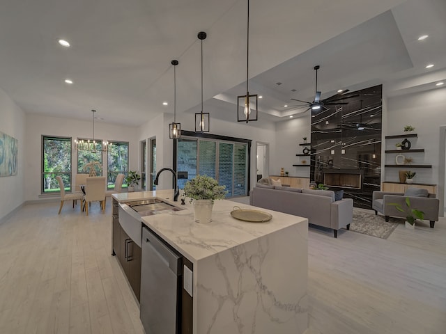 kitchen featuring dishwasher, an island with sink, a large fireplace, light stone countertops, and pendant lighting