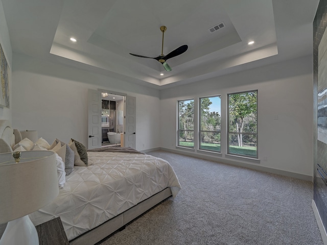 carpeted bedroom with ceiling fan, a raised ceiling, and ensuite bath