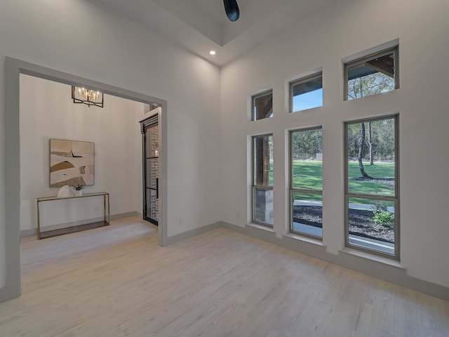 unfurnished room with light hardwood / wood-style floors, a notable chandelier, and a towering ceiling