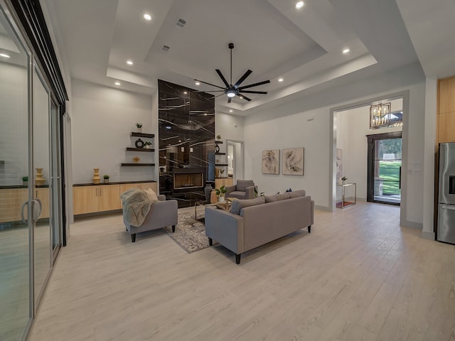 living room featuring ceiling fan with notable chandelier, a fireplace, light hardwood / wood-style floors, and a raised ceiling