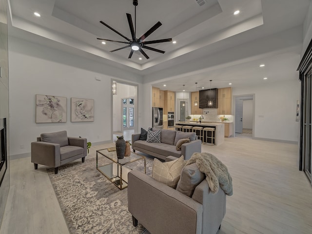 living room featuring sink, a tray ceiling, light wood-type flooring, and ceiling fan