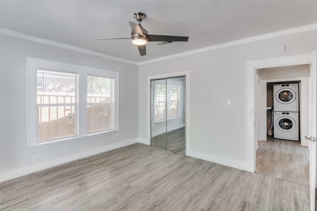 unfurnished room featuring light hardwood / wood-style flooring, crown molding, stacked washer and dryer, and ceiling fan