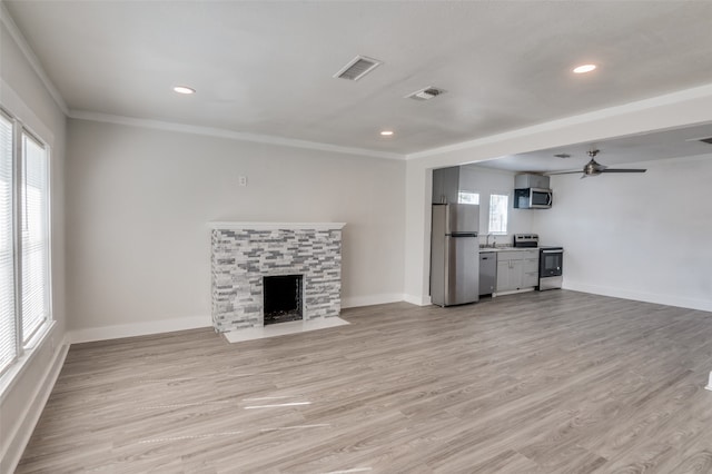 unfurnished living room featuring sink, crown molding, a fireplace, light hardwood / wood-style floors, and ceiling fan