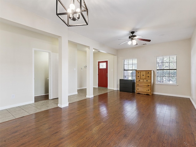 unfurnished living room with wood-type flooring, ceiling fan with notable chandelier, and decorative columns