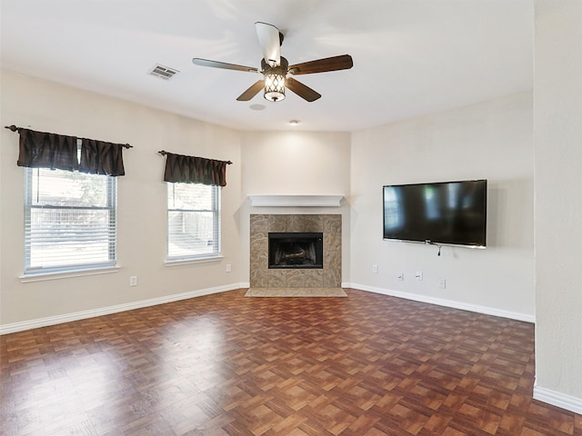 unfurnished living room with dark parquet flooring, a tiled fireplace, and ceiling fan