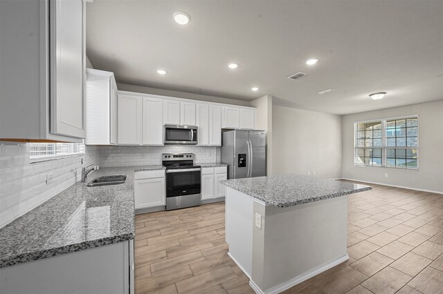 kitchen featuring sink, a center island, stainless steel appliances, white cabinets, and light stone counters