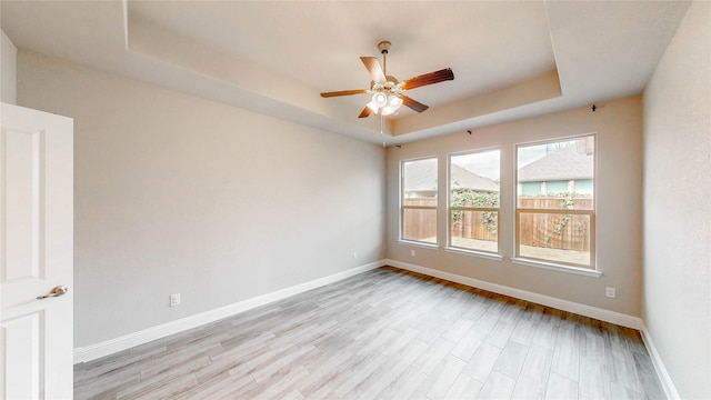 empty room with a tray ceiling, light wood-type flooring, and ceiling fan