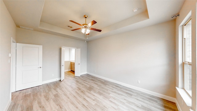 unfurnished bedroom featuring light hardwood / wood-style floors, a raised ceiling, and multiple windows