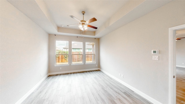 spare room featuring light hardwood / wood-style flooring, a tray ceiling, and ceiling fan