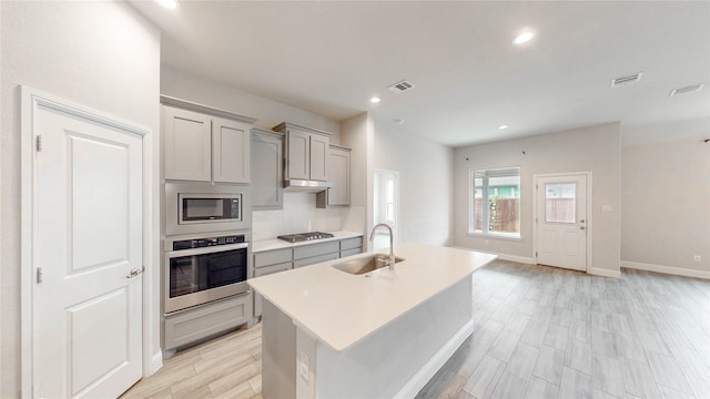 kitchen with an island with sink, stainless steel appliances, sink, and gray cabinetry