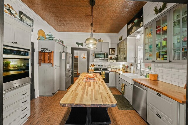 kitchen featuring sink, wooden counters, hardwood / wood-style floors, pendant lighting, and appliances with stainless steel finishes