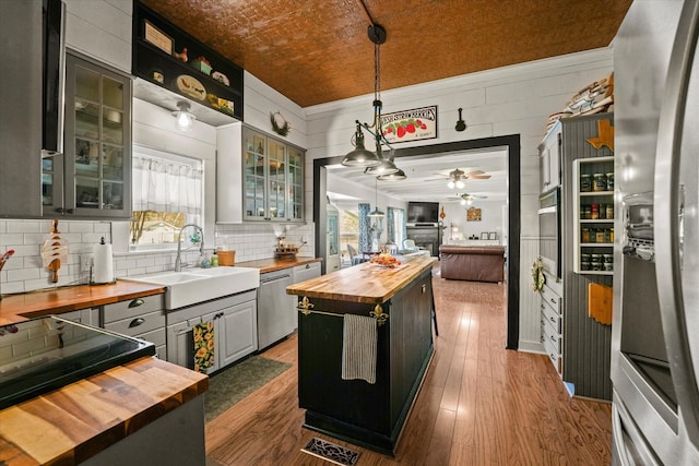 kitchen with pendant lighting, wood counters, sink, a kitchen island, and stainless steel appliances