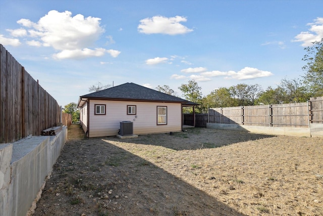 back of house with central air condition unit, a fenced backyard, and a shingled roof