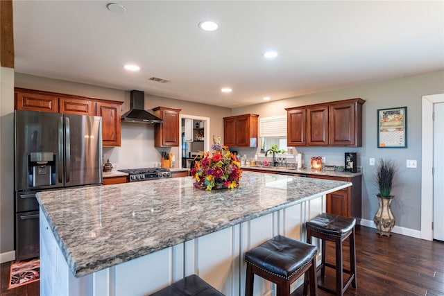 kitchen featuring wall chimney range hood, appliances with stainless steel finishes, a kitchen bar, a center island, and dark hardwood / wood-style floors