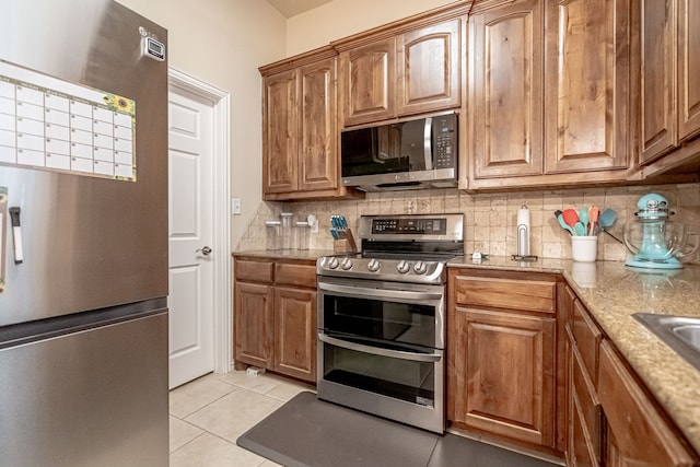 kitchen with light stone countertops, appliances with stainless steel finishes, light tile patterned floors, and decorative backsplash