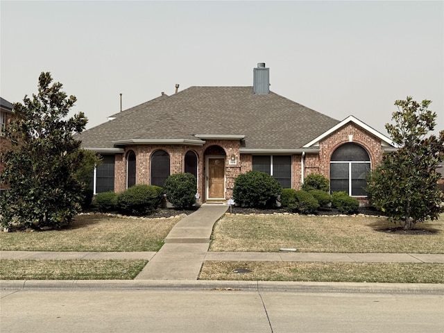 ranch-style house featuring a front yard, brick siding, roof with shingles, and a chimney