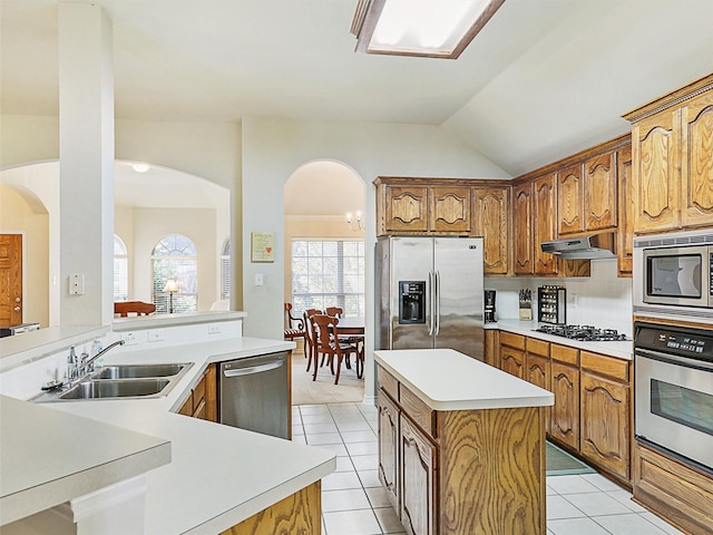 kitchen with under cabinet range hood, a kitchen island, stainless steel appliances, arched walkways, and light tile patterned floors