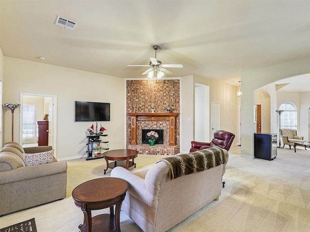 living area featuring visible vents, light carpet, arched walkways, a brick fireplace, and ceiling fan