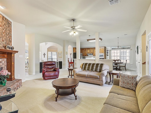 living room with a ceiling fan, baseboards, visible vents, arched walkways, and light carpet