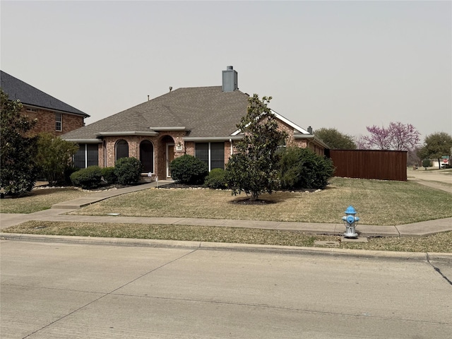 view of front of house featuring a front yard, brick siding, roof with shingles, and a chimney