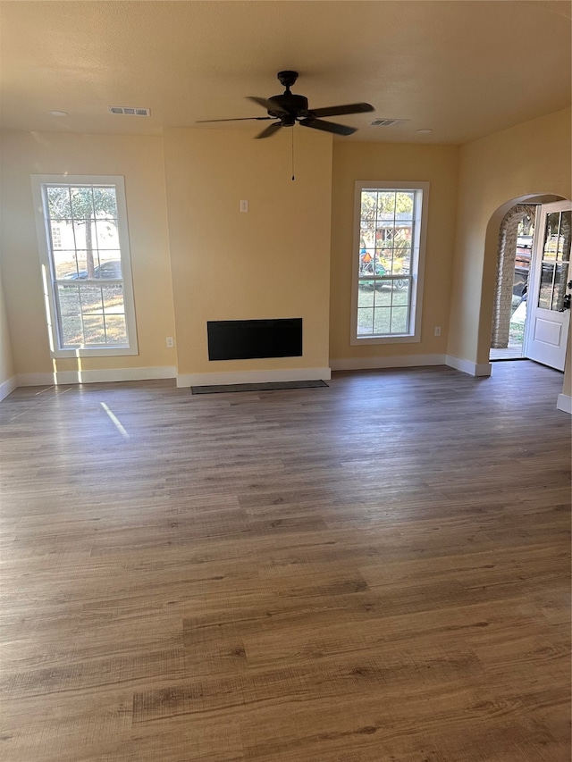 unfurnished living room featuring ceiling fan, a healthy amount of sunlight, and dark hardwood / wood-style flooring