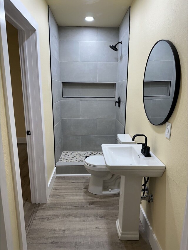 bathroom with toilet, hardwood / wood-style floors, and tiled shower