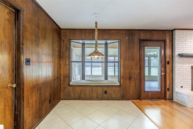 unfurnished dining area with a fireplace, wood walls, light hardwood / wood-style flooring, and crown molding