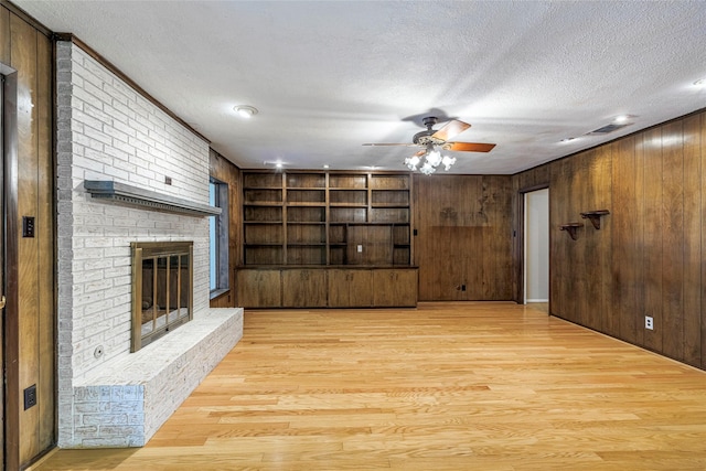 living room featuring wood walls, a fireplace, light hardwood / wood-style floors, and a textured ceiling