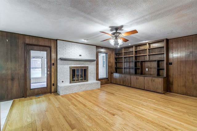 unfurnished living room featuring a brick fireplace, a textured ceiling, light hardwood / wood-style flooring, and wood walls