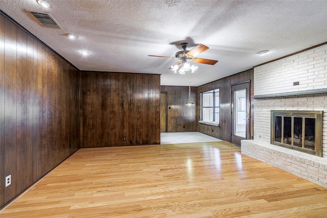 unfurnished living room with a textured ceiling, light hardwood / wood-style floors, a brick fireplace, and wooden walls