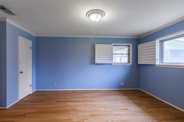 empty room featuring a textured ceiling, light wood-type flooring, and crown molding