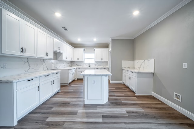 kitchen with a kitchen island, white cabinetry, light hardwood / wood-style floors, crown molding, and light stone counters