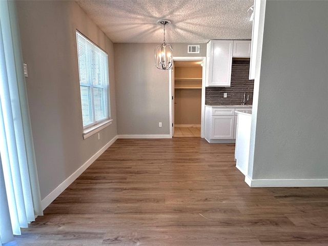 unfurnished dining area with light hardwood / wood-style flooring, a textured ceiling, and a notable chandelier