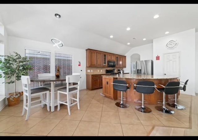 kitchen with lofted ceiling, light tile patterned floors, a breakfast bar, black appliances, and light stone counters