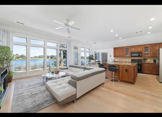 living room featuring a water view, light hardwood / wood-style floors, and ceiling fan