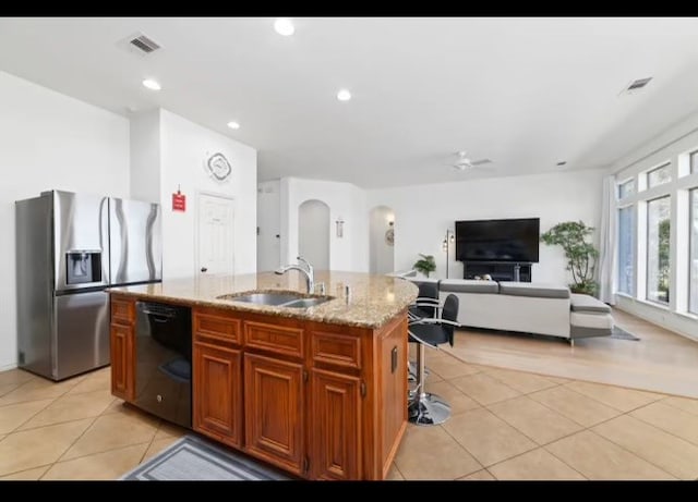 kitchen featuring black dishwasher, sink, light tile patterned flooring, an island with sink, and stainless steel fridge with ice dispenser