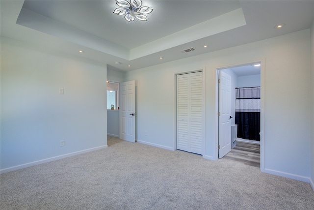 unfurnished bedroom with connected bathroom, a closet, a raised ceiling, and light colored carpet