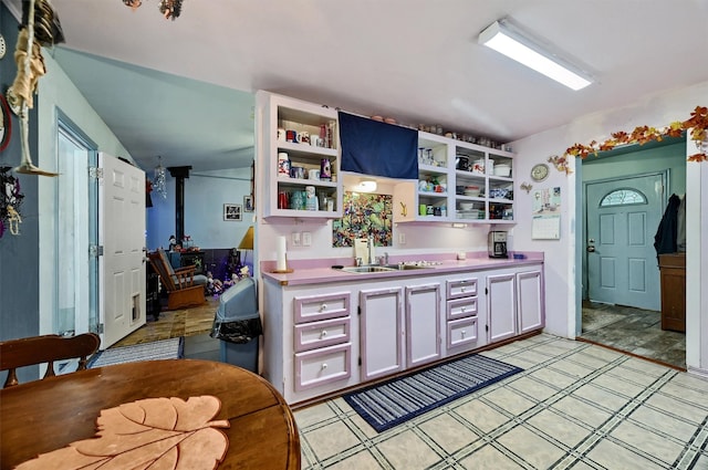 kitchen with vaulted ceiling, white cabinetry, sink, and a wood stove