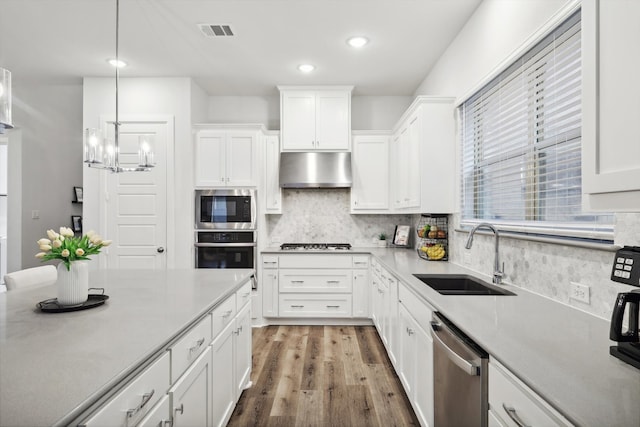 kitchen featuring stainless steel appliances, range hood, sink, decorative light fixtures, and white cabinets