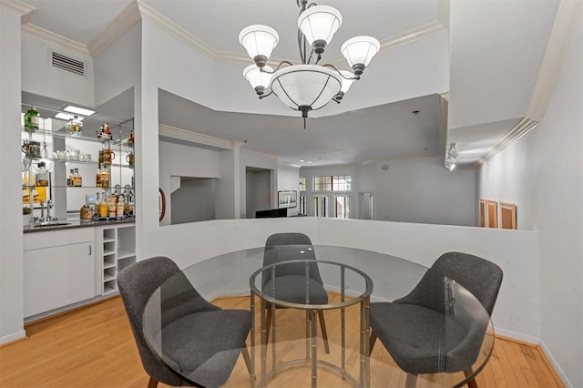 dining area with light hardwood / wood-style floors, crown molding, indoor wet bar, and an inviting chandelier