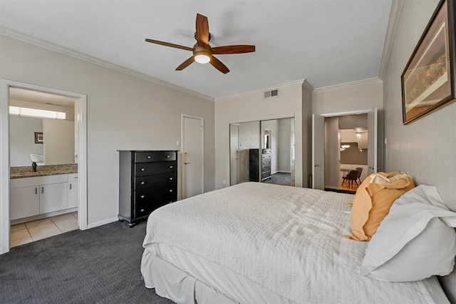 carpeted bedroom with a closet, crown molding, ensuite bathroom, and ceiling fan