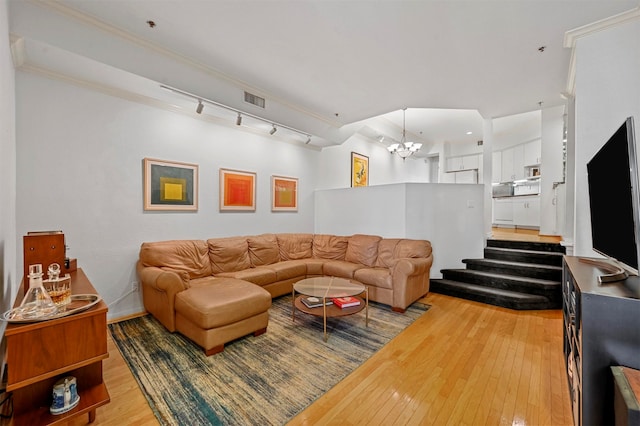 living room featuring rail lighting, a notable chandelier, ornamental molding, and light wood-type flooring