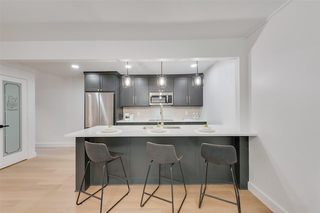 kitchen with pendant lighting, a breakfast bar, stainless steel appliances, decorative backsplash, and light wood-type flooring