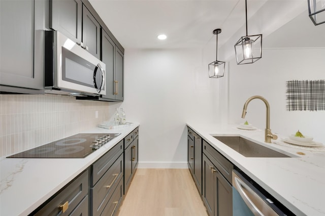 kitchen with sink, light hardwood / wood-style flooring, appliances with stainless steel finishes, hanging light fixtures, and light stone counters