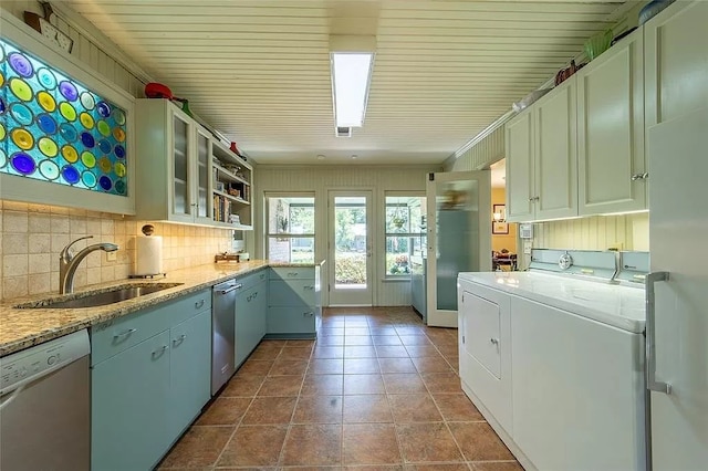 kitchen with white dishwasher, sink, light stone countertops, white cabinetry, and washer and dryer