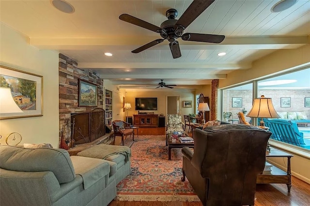 living room with beam ceiling, a stone fireplace, wood-type flooring, and ceiling fan