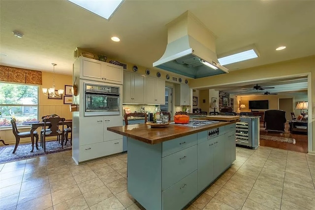 kitchen with oven, a kitchen island, island range hood, butcher block counters, and white cabinets