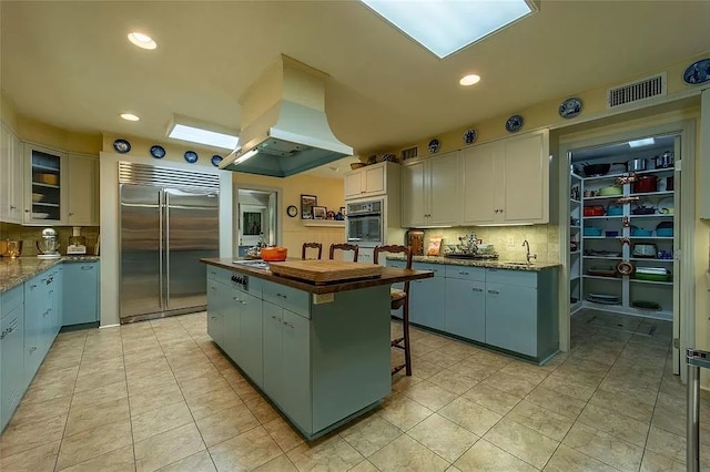 kitchen with tasteful backsplash, island range hood, a skylight, built in fridge, and a center island